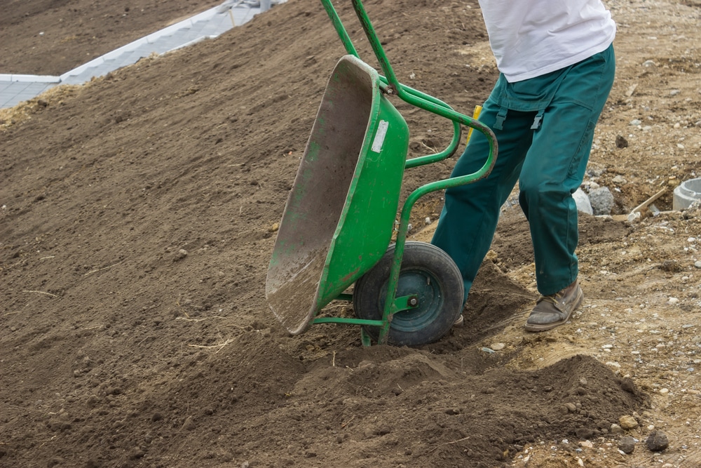 man using a green wheelbarrow to transport soil